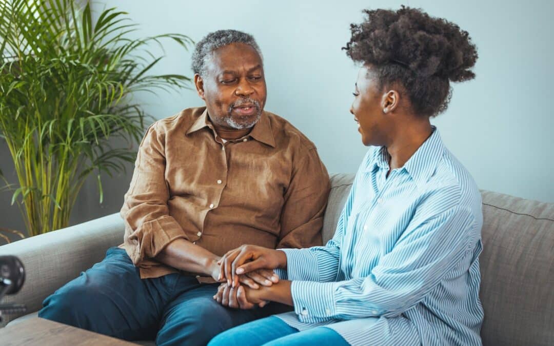 Senior Man and Daughter Sit on Couch Holding Hands_Ciel Senior Living